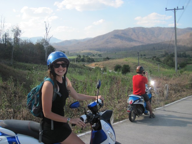 A traveller in a helmet on a scooter beside a mountain road